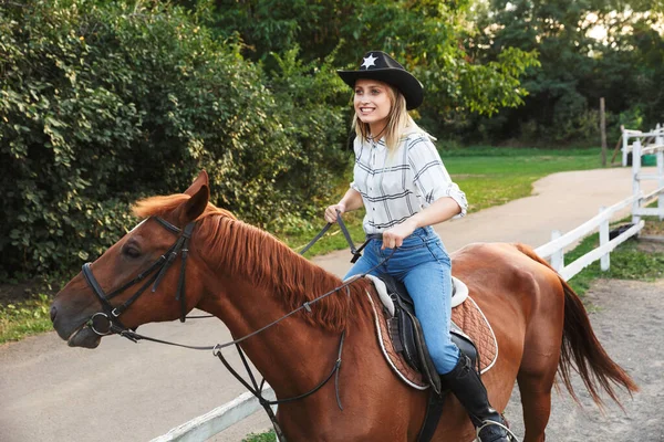 Sonriente joven rubia atractiva montando un caballo —  Fotos de Stock