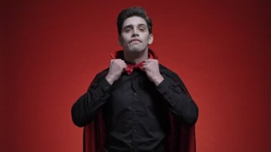 Siyah cadılar bayramı kostümü giymiş vampir adam papyonunu, yakasını, saçlarını ve dişlerini kırmızı duvarın üstüne sabitliyor.