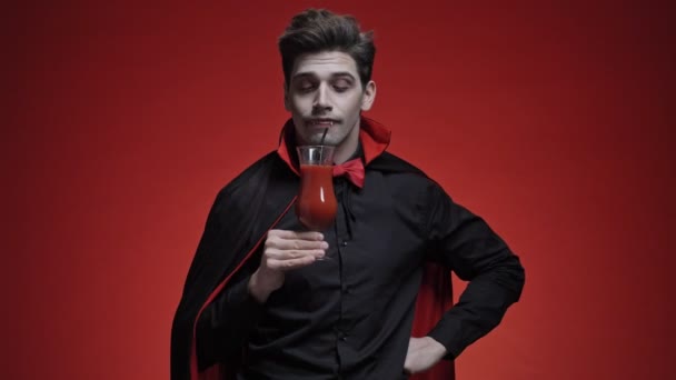 恐怖的吸血鬼男人 长着黑色的长牙 穿着黑色的长裙 尝着西红柿鸡尾酒 不喜欢隔着红墙隔离开来 — 图库视频影像