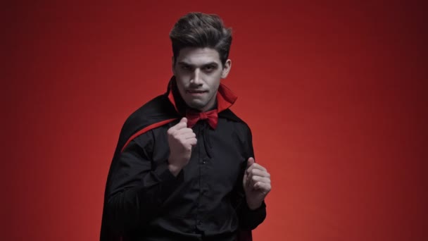身穿黑衣 头戴尖牙 血淋淋的吸血鬼在红墙上跳舞 面带微笑 — 图库视频影像