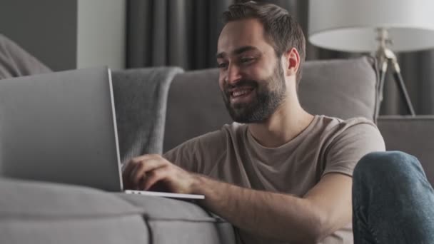 Jovem Sorridente Satisfeito Está Usando Seu Laptop Sentado Casa Sala — Vídeo de Stock