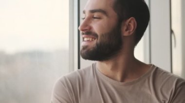 Yakışıklı bir genç adam pencereye bakıyor. Evde oturuyor.