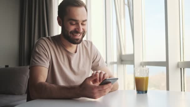 Ein Lachender Glücklicher Junger Mann Sitzt Hause Mit Seinem Smartphone — Stockvideo