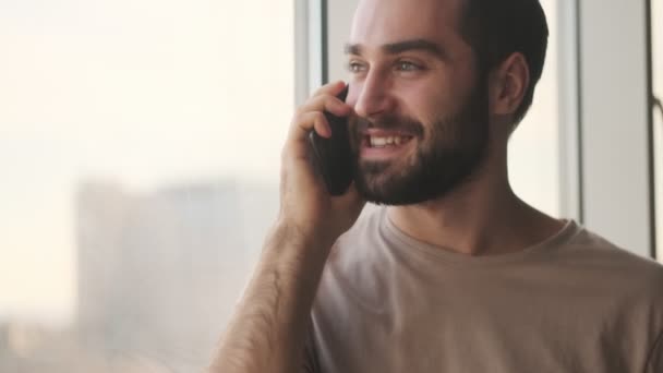 Jovem Sorridente Está Falando Seu Smartphone Casa Perto Janela — Vídeo de Stock