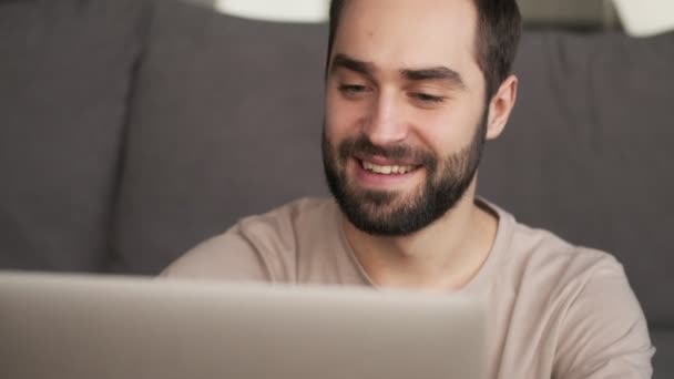 Ein Lächelnder Attraktiver Junger Mann Sitzt Mit Seinem Laptop Hause — Stockvideo