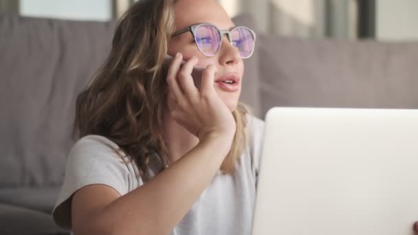 若い正の女性屋内で自宅でラップトップコンピュータを使用して話す携帯電話 — ストック動画