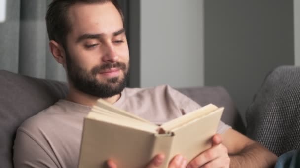 Jovem Positivo Atraente Está Lendo Livro Sentado Casa Sofá Sala — Vídeo de Stock