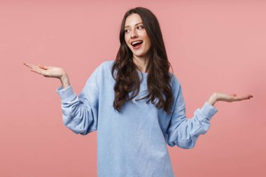 Uzun kahverengi saçlı, gülümseyen ve kollarını kaldıran çekici bir kadın resmi pembe arka planda izole edilmiş.