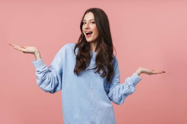 Uzun kahverengi saçlı, gülümseyen ve kollarını kaldıran çekici bir kadın resmi pembe arka planda izole edilmiş.