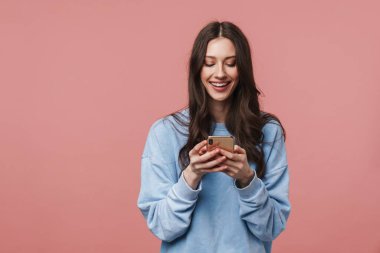 Gülümseyen ve pembe arka planda izole akıllı telefon kullanan mutlu bir kadın görüntüsü.