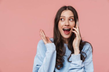 Pembe arka planda, uzun kahverengi saçlı, gülümseyen ve cep telefonuyla konuşan çekici bir kadın resmi.