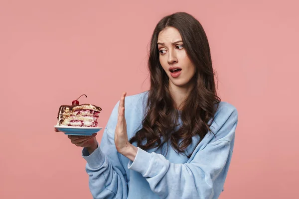 Obraz Niezadowolonej Brunetki Wykonującej Gest Odmowy Trzymającej Kawałek Ciasta Różowym — Zdjęcie stockowe