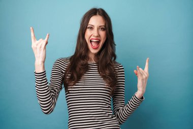 Çizgili kazaklı, mutlu genç bir kadının mavi duvarın üzerinde parmakları izole bir şekilde boynuz hareketi.