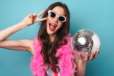 Mavi duvarda izole edilmiş disko topuyla poz verirken barış işareti yapan neşeli genç bir kadının fotoğrafı