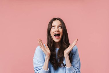 Pembe arka planda uzun kahverengi saçlı, gülümseyen ve ellerini kaldıran çekici bir kadın resmi.