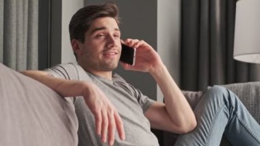Evde cep telefonuyla konuşan yakışıklı, konsantre bir adam.