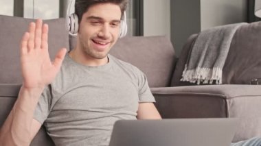 Evde mutlu bir adam var. Bilgisayar kullanıyor. Kulaklıkla video konuşmaları yapıyor.