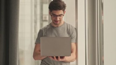 Memnuniyet verici olumlu adam evde dizüstü bilgisayar kullanarak pencereye bakıyor.