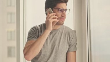 Evde konsantre olmuş bir adam cep telefonuyla konuşuyor.