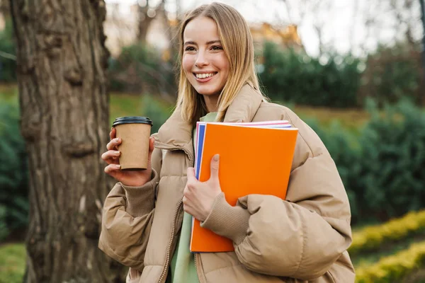 Elinde Egzersiz Kitapları Olan Parkta Yürürken Kahve Içen Gülümseyen Genç — Stok fotoğraf