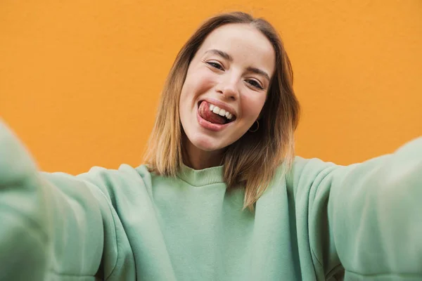 Portret Zabawnej Młodej Kobiety Robiącej Selfie Wystającym Językiem Wyizolowanym Żółtym — Zdjęcie stockowe