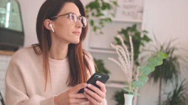 Kulaklıklı hoş bir kadın, rahat bir kafede otururken akıllı telefonunu kullanıyor.