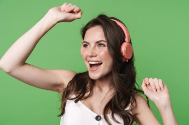 Yeşil arka planda izole edilmiş kablosuz kulaklık kullanırken dans eden neşeli bir kadın görüntüsü