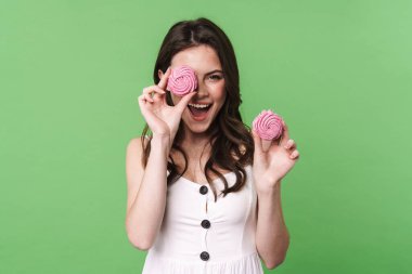 Gülümseyen ve yeşil arka planda izole edilmiş şekerlemeleri tutan heyecanlı genç bir kadın görüntüsü