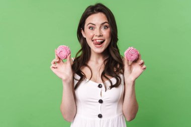 Gülümseyen ve yeşil arka planda izole edilmiş şekerlemeleri tutan heyecanlı genç bir kadın görüntüsü