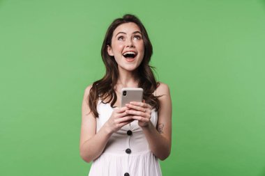 Yeşil arka planda izole edilmiş, gülümseyen ve cep telefonu kullanan heyecanlı çekici bir kadın görüntüsü