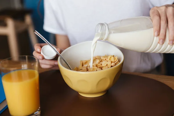 台所のテーブルに座っている間に健康的な朝食を持っている若い女性の閉じる シリアルにミルクを注ぐ — ストック写真