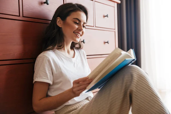 Atractiva Joven Morena Sonriente Leyendo Libro Mientras Está Sentada Suelo — Foto de Stock