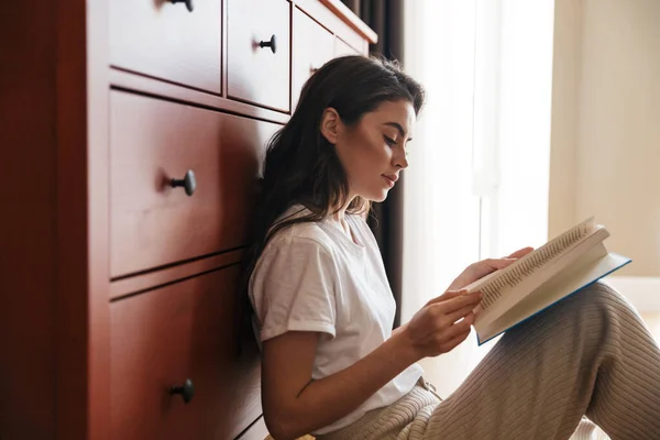 Jovem Morena Atraente Lendo Livro Enquanto Senta Chão Inclina Armário — Fotografia de Stock