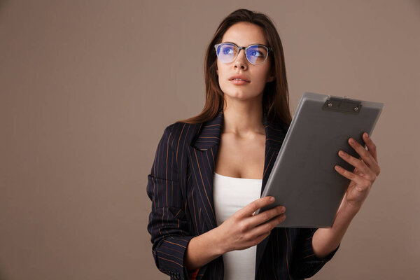 Photo of focused businesswoman in eyeglasses posing with clipboard isolated over grey background