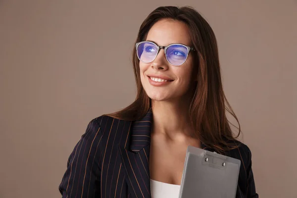 Photo of attractive businesswoman in eyeglasses smiling and posing with clipboard isolated over grey background