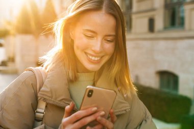 Şehir caddesinde yürürken cep telefonu kullanan ve gülümseyen beyaz kadın portresi