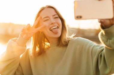 Neşeli kadın portresi barış işareti yapıyor ve gezinirken cep telefonuyla selfie çekiyor.