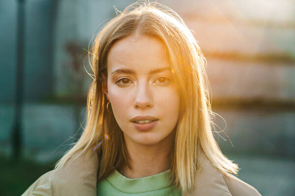 Portrait closeup of young blonde woman posing and looking at camera while walking in park