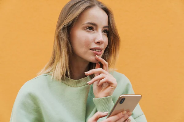 Portret Myślącej Blondynki Korzystającej Telefonu Komórkowego Spoglądającej Górę Żółte Tło — Zdjęcie stockowe