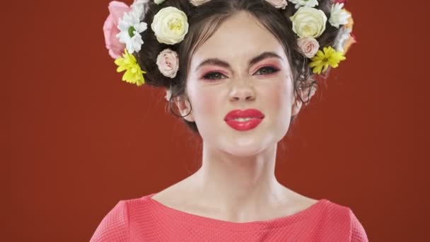 Смешная Эмоциональная Брюнетка Удивительной Цветочной Прической Демонстрирует Язык Изолированный Красном — стоковое видео
