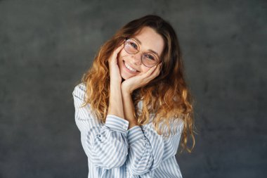 Gözlüklü, mutlu ve çekici bir kadının görüntüsü. Gri duvarda izole bir şekilde gülümseyen ve kameraya poz veren.