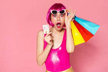 Pembe arka planda alışveriş torbaları ve kredi kartı taşıyan heyecanlı genç bir kız resmi