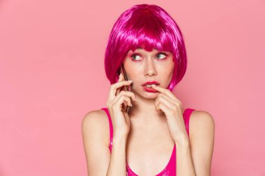 Pembe arka planda cep telefonuyla konuşan peruk takan güzel bir kız resmi.