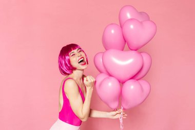 Heyecanlı, peruklu, balonlu güzel bir kadın resmi ve pembe arka planda izole edilmiş bir jest yapıyor.