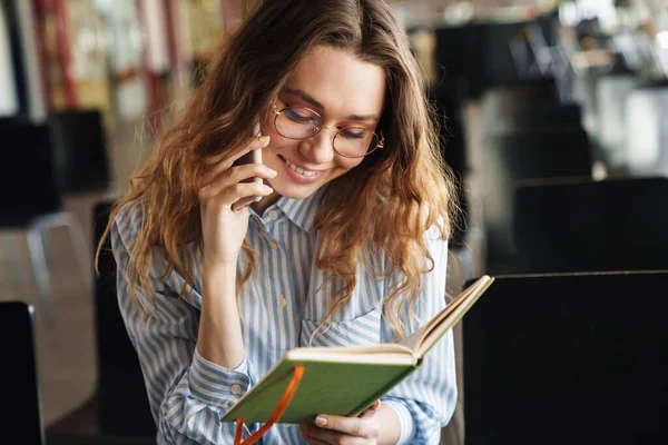 Imagem Jovem Alegre Falando Celular Segurando Planejador Enquanto Sentado Sala — Fotografia de Stock