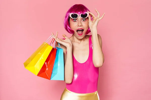 照片中 兴奋的女孩戴着假发和太阳镜尖叫着 提着粉色背景的购物袋 — 图库照片
