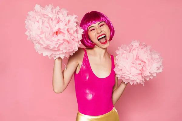 Image of excited nice woman wearing wig screaming and dancing with pom-poms isolated over pink background