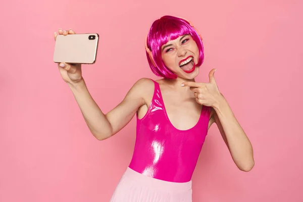 ヘッドフォンで指を指し ピンクの背景に隔離された携帯電話で自撮りの喜びの女性のイメージ — ストック写真