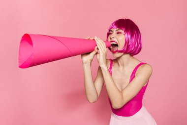 Pembe arka planda izole edilmiş, hoparlörden bağıran peruklu, heyecanlı genç bir kadın görüntüsü.
