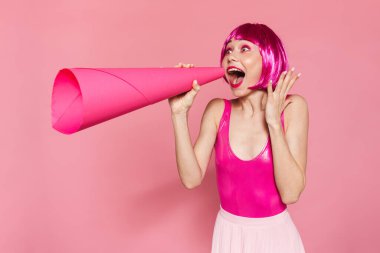 Pembe arka planda izole edilmiş, hoparlörden bağıran peruklu, heyecanlı genç bir kadın görüntüsü.